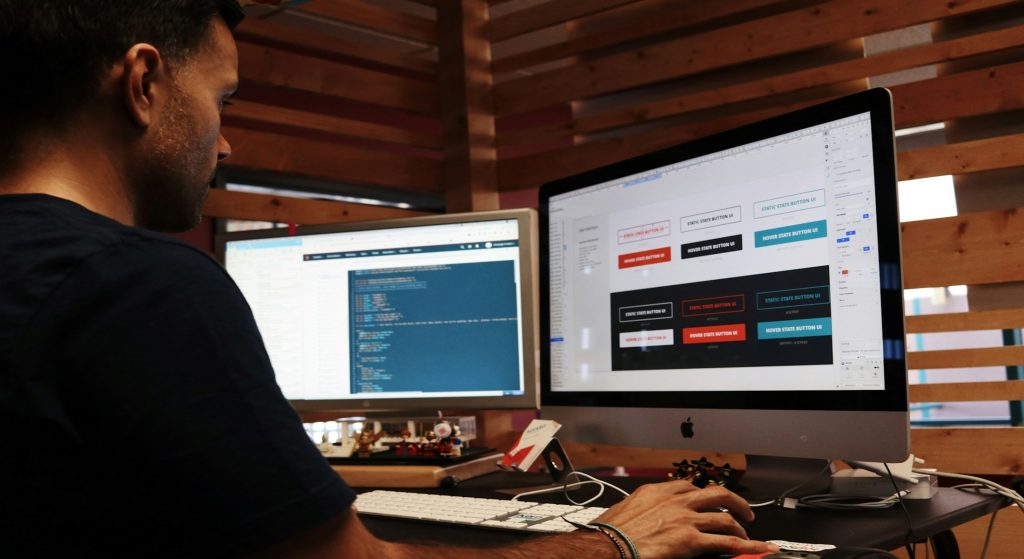 A person working on web design at a desk with two computer monitors.